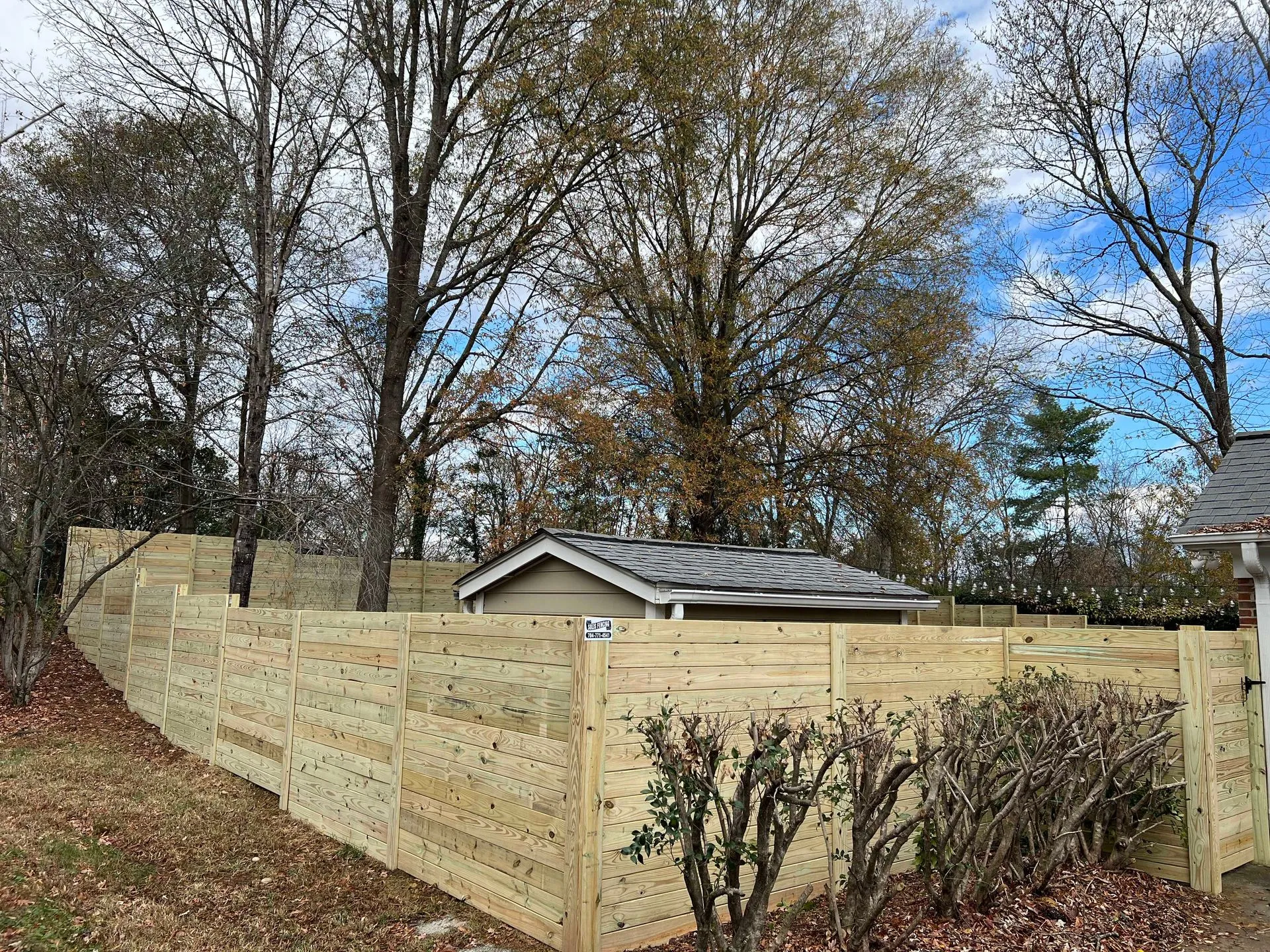 Wooden fence surrounding trees and small building.