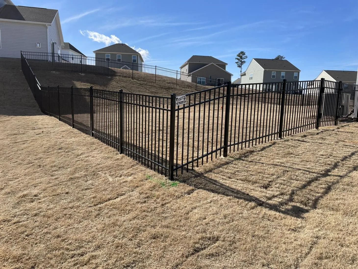 Black metal fence on sloped grassy yard.