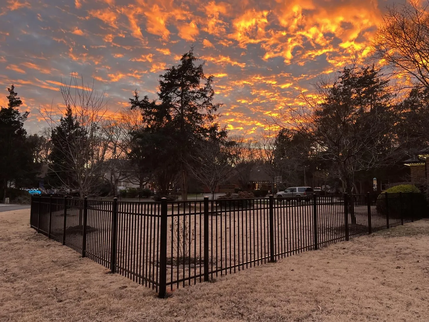Sunset sky over fenced grassy area.
