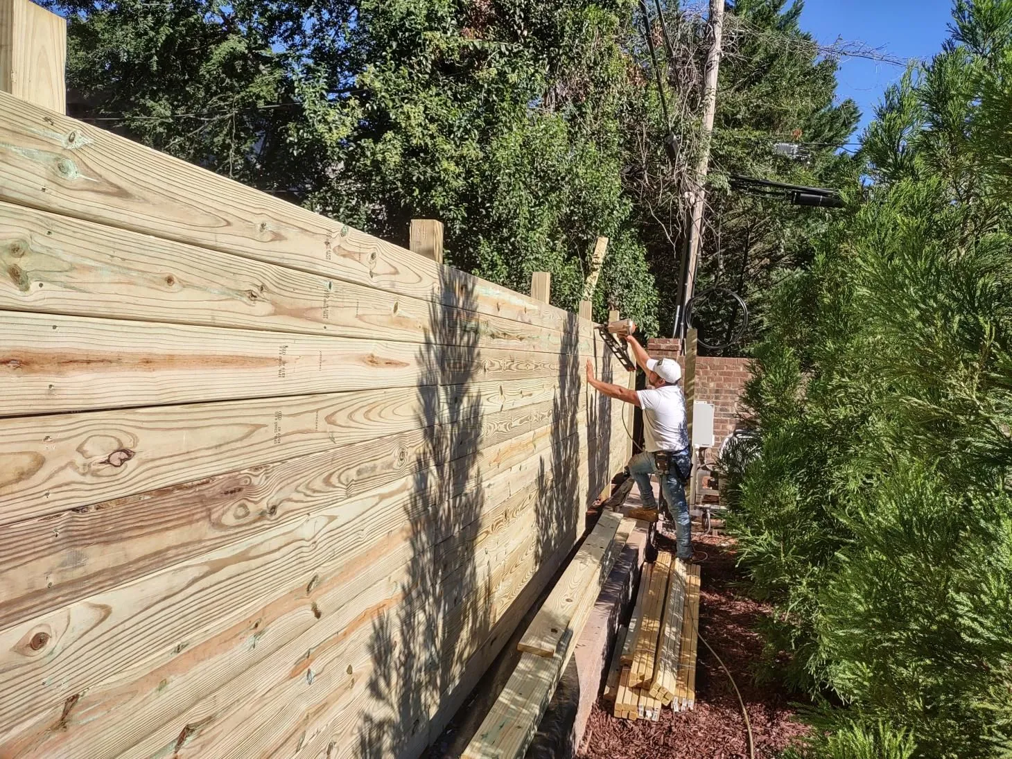 Person building a wooden fence outdoors.