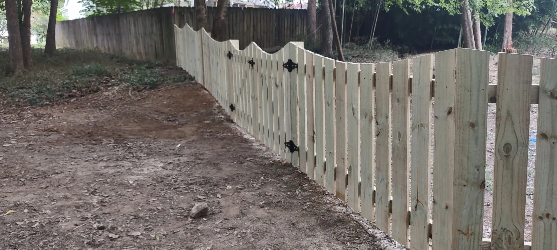 Wooden fence along dirt path in forest.