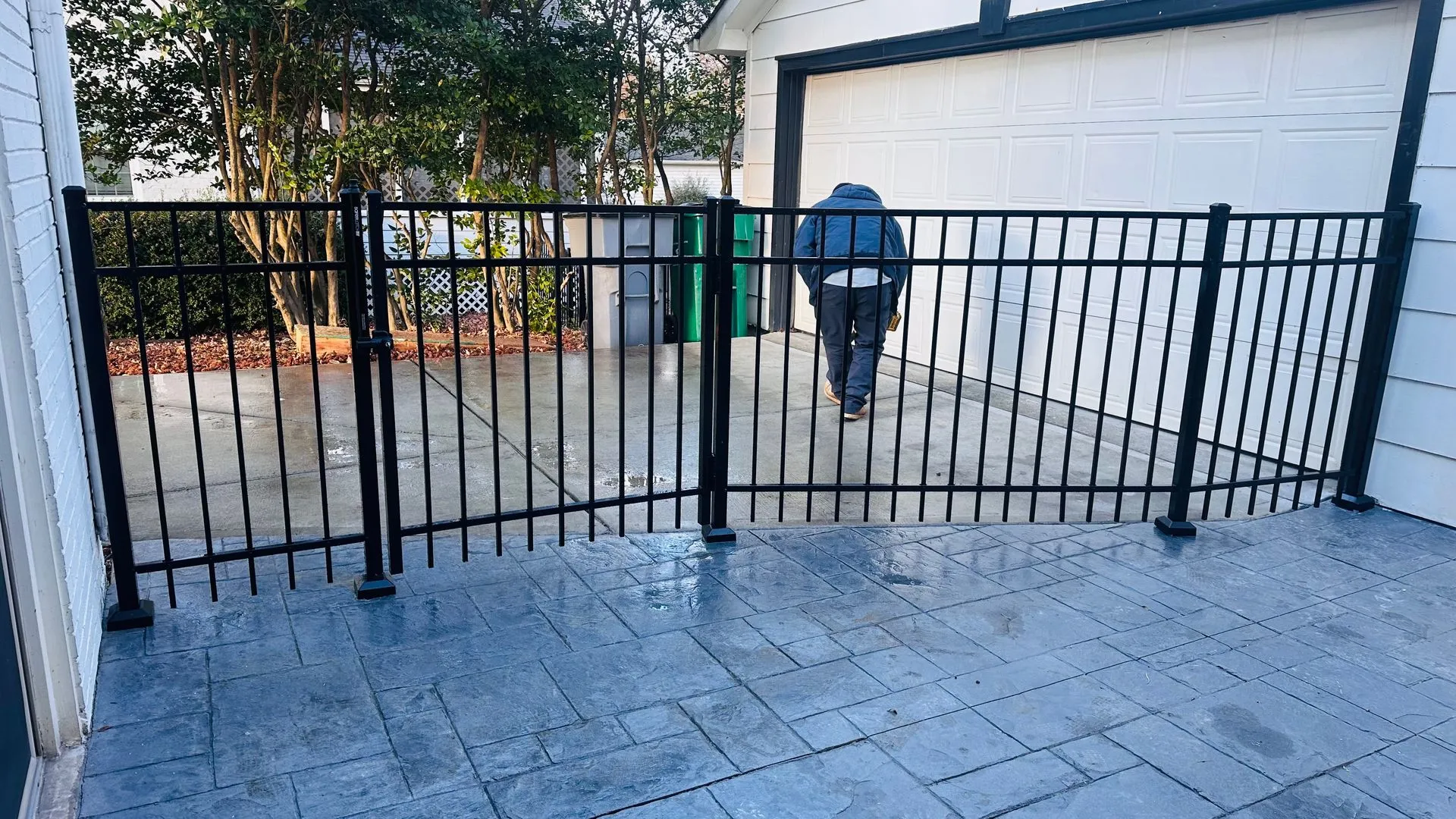 Man walking on driveway behind black fence.
