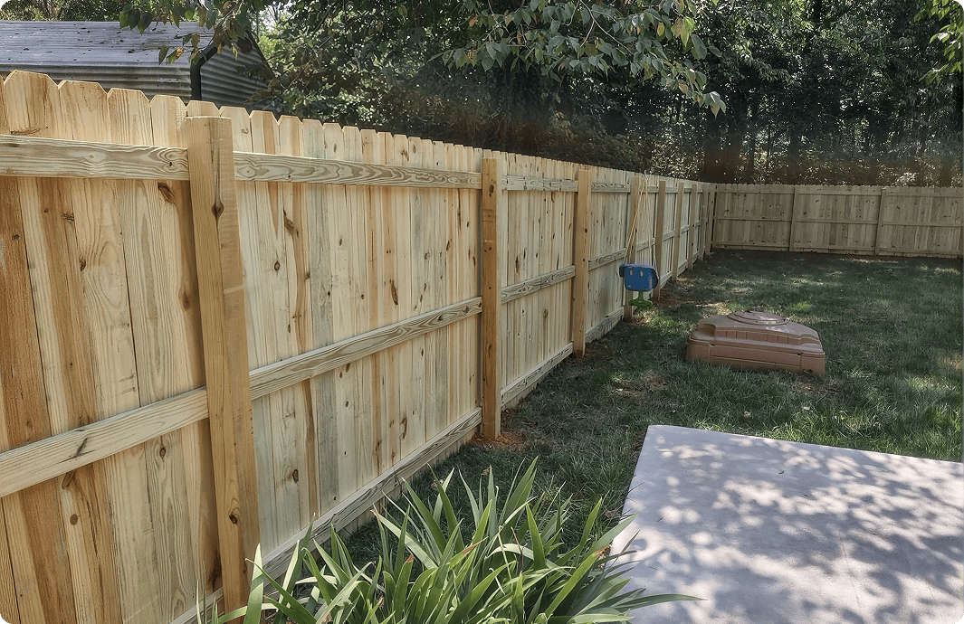 Wooden fence enclosing grassy backyard area.