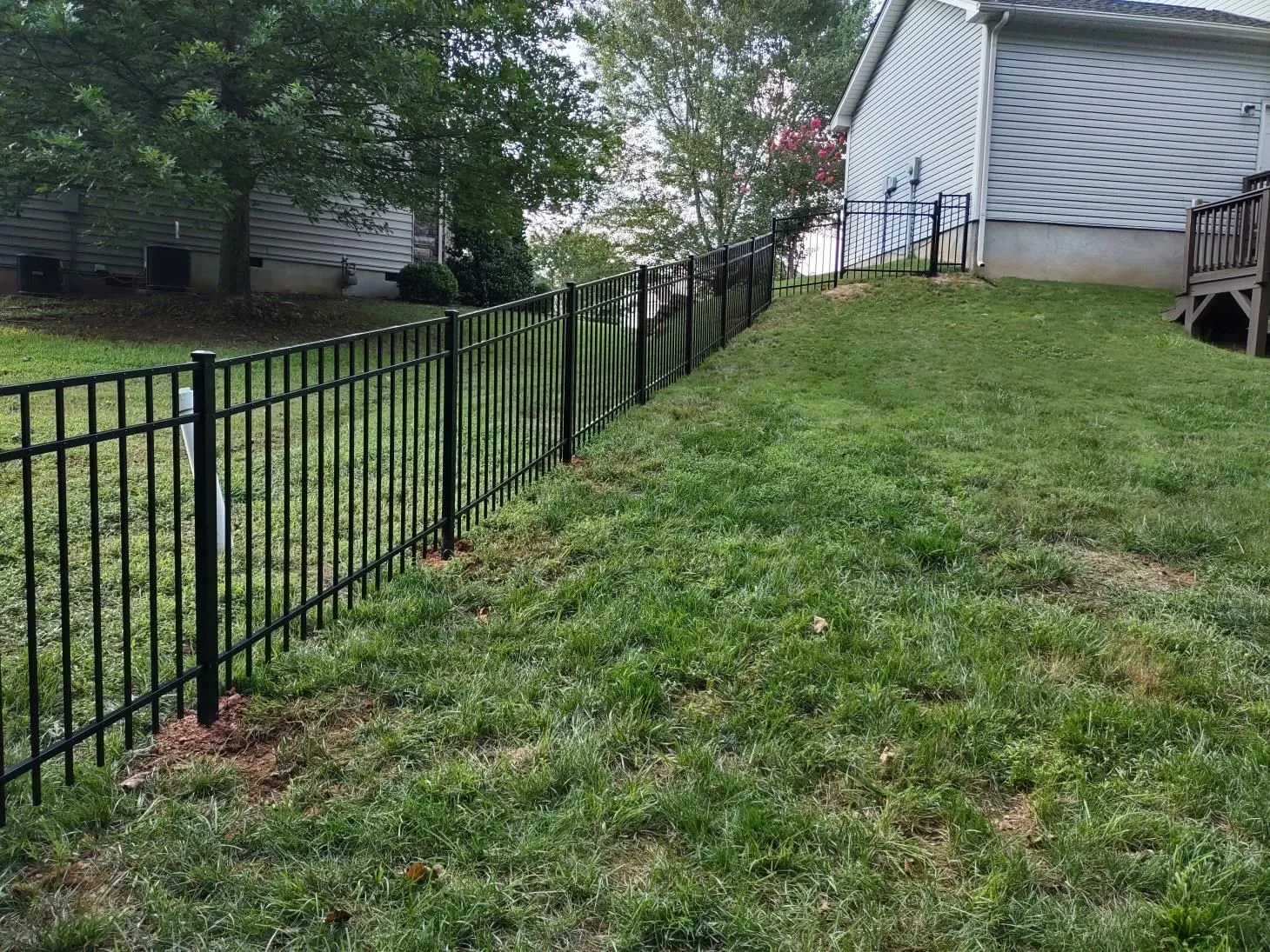 Black metal fence on sloped grassy yard.