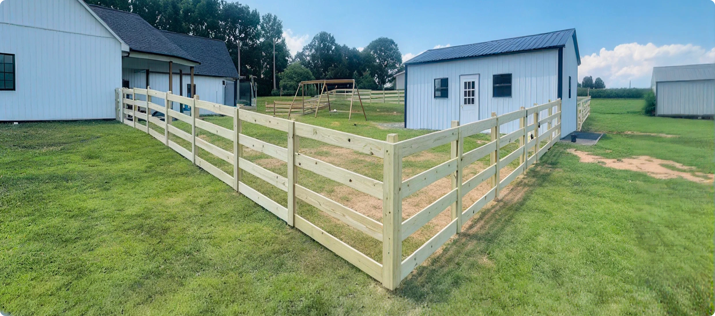 Wooden fence between two white farm buildings.