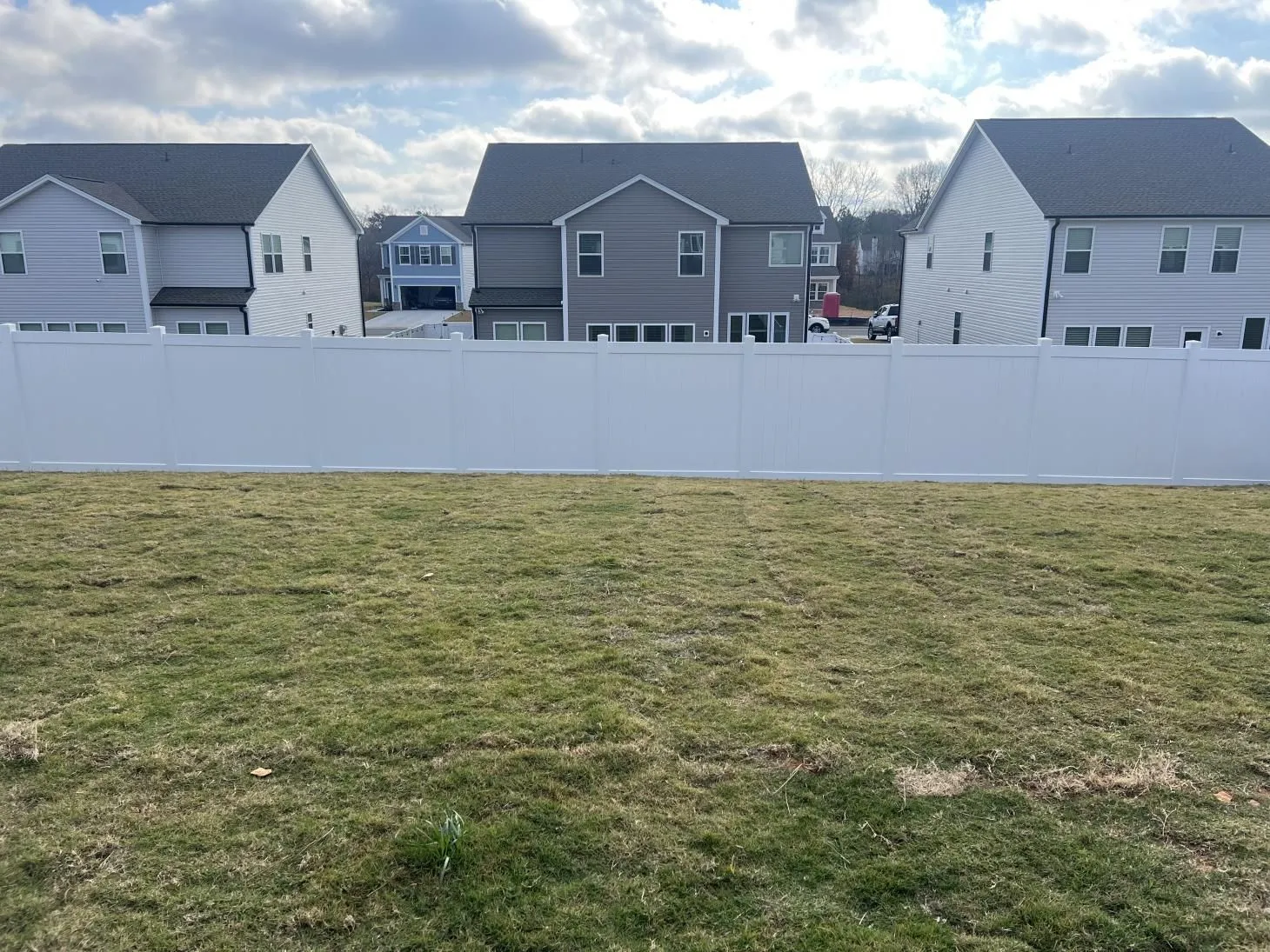 Suburban houses behind white fence, cloudy sky.