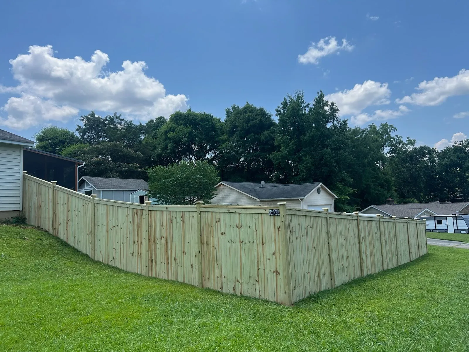 Wooden fence surrounding backyard under blue sky.