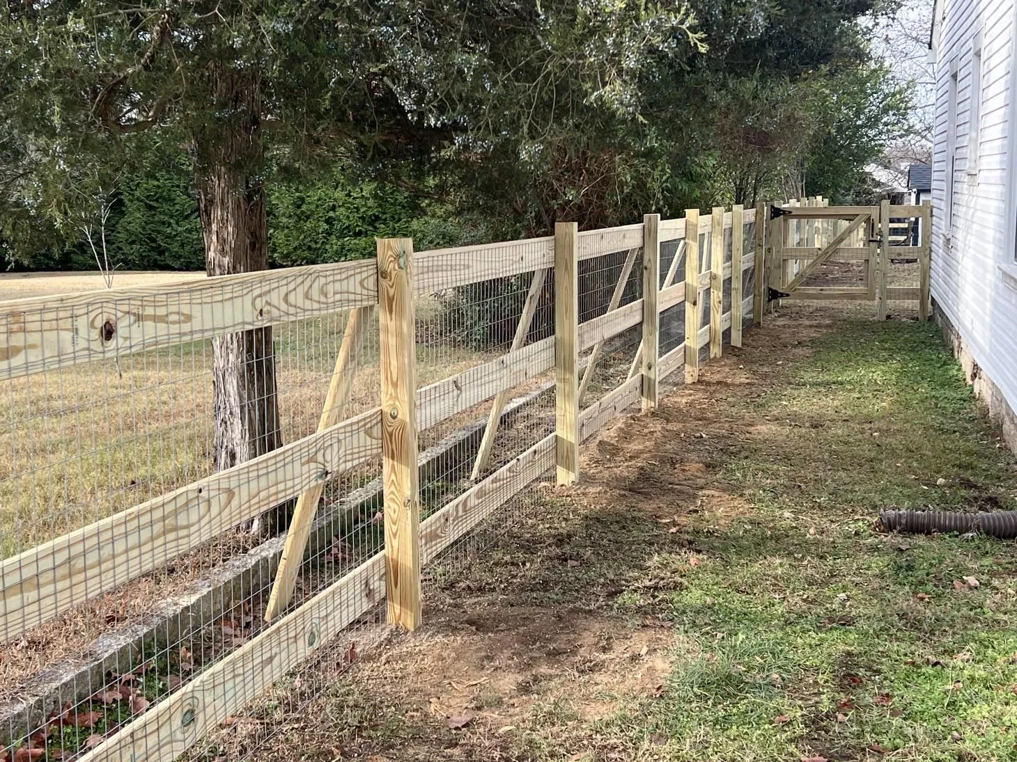 Wooden fence beside a house and trees.