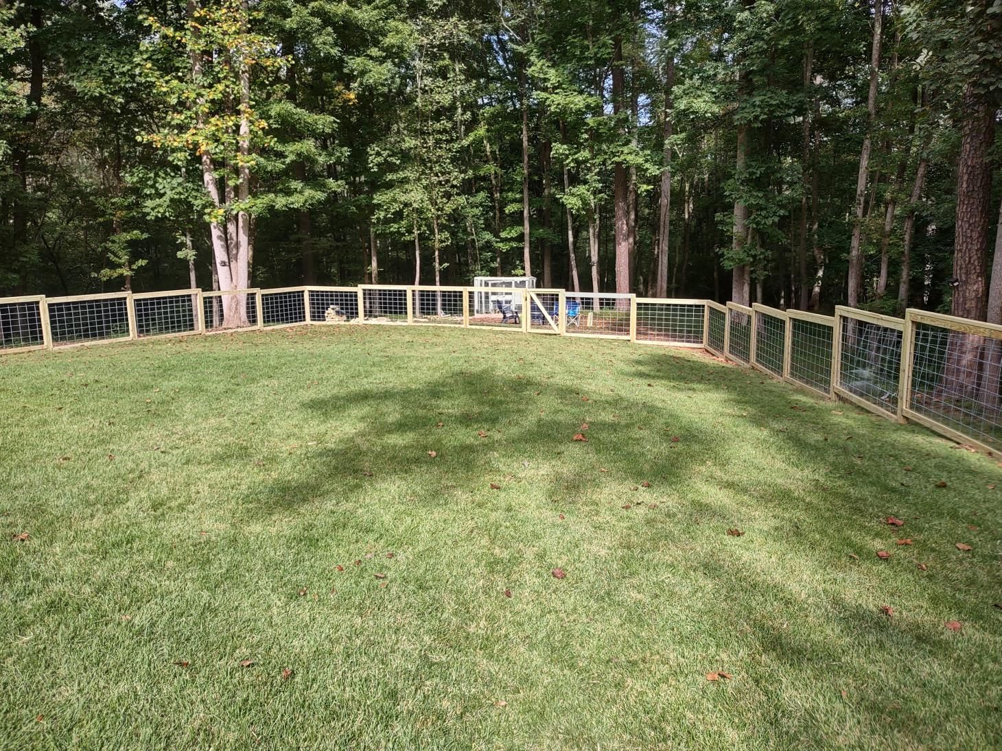 Fenced grassy area surrounded by trees.