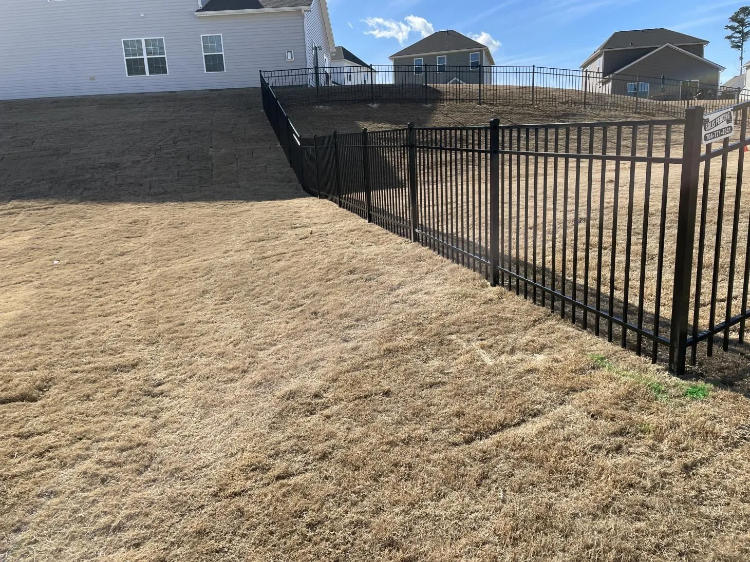 Sloped yard with black metal fence.