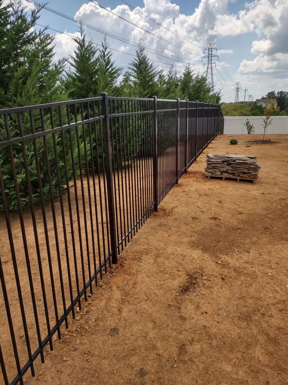 Metal fence beside trees and dirt path.