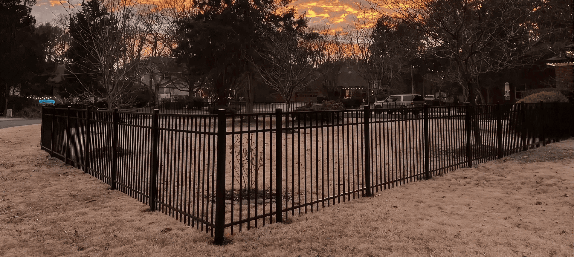Fenced yard with sunset and trees.