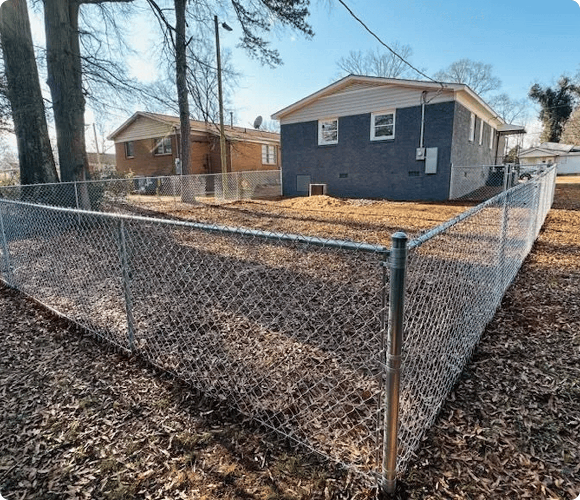 Fenced backyard with trees and brick house.