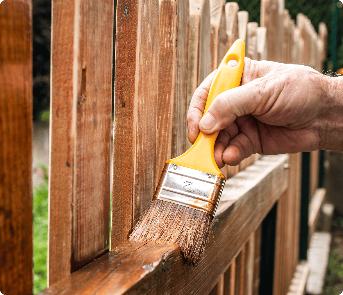 Hand painting wooden fence with brush.