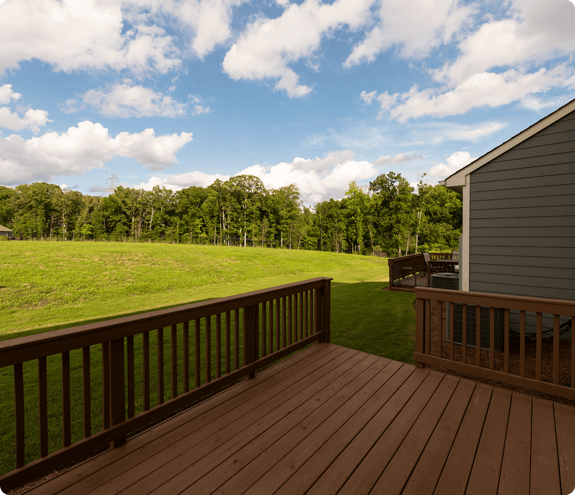 Wooden deck overlooking grassy field and trees.