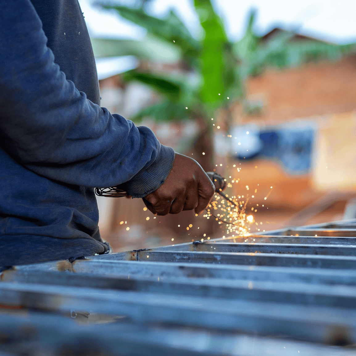 Person welding metal outdoors, sparks flying.