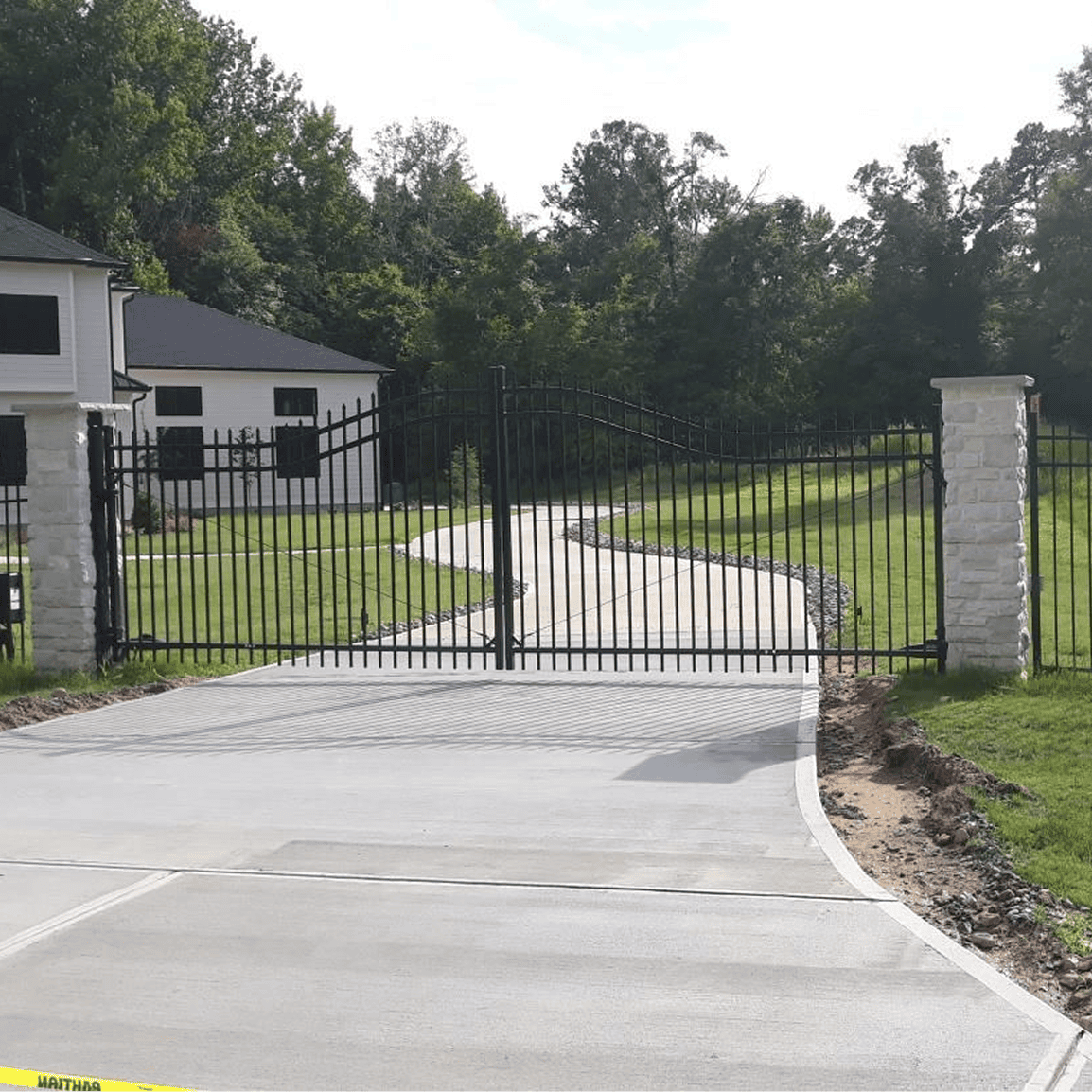 Driveway with iron gate and lush greenery.