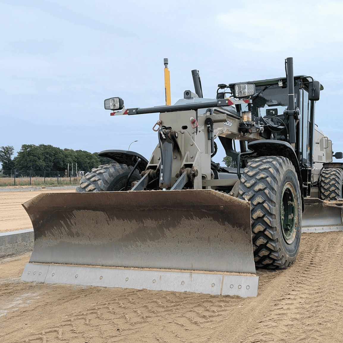 Construction grader leveling sandy ground surface.